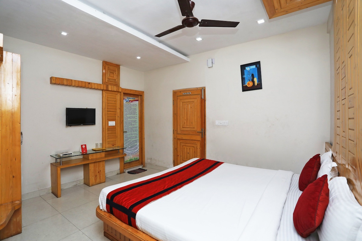 A hotel room with a bed, wooden wardrobe, desk, and a television.