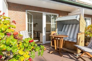 A patio with a wicker chair, a striped sofa, and a table. - Wellness Oasis Holiday Home 06 (Wenningstedt)