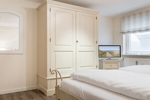 A bedroom with a double bed, a wardrobe, a television on a stand, and a window with curtains. - Wellness Oasis Holiday Home 06 (Wenningstedt)
