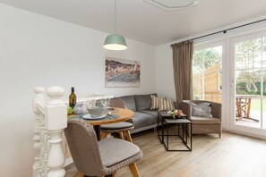 A modern living room with a dining area, a sofa, a coffee table, and a large window with curtains. - Wellness Oasis Holiday Home 06 (Wenningstedt)