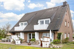A two-story house with a sloped roof, a stone foundation, and a patio with outdoor furniture. - Wellness Oasis Holiday Home 06 (Wenningstedt)