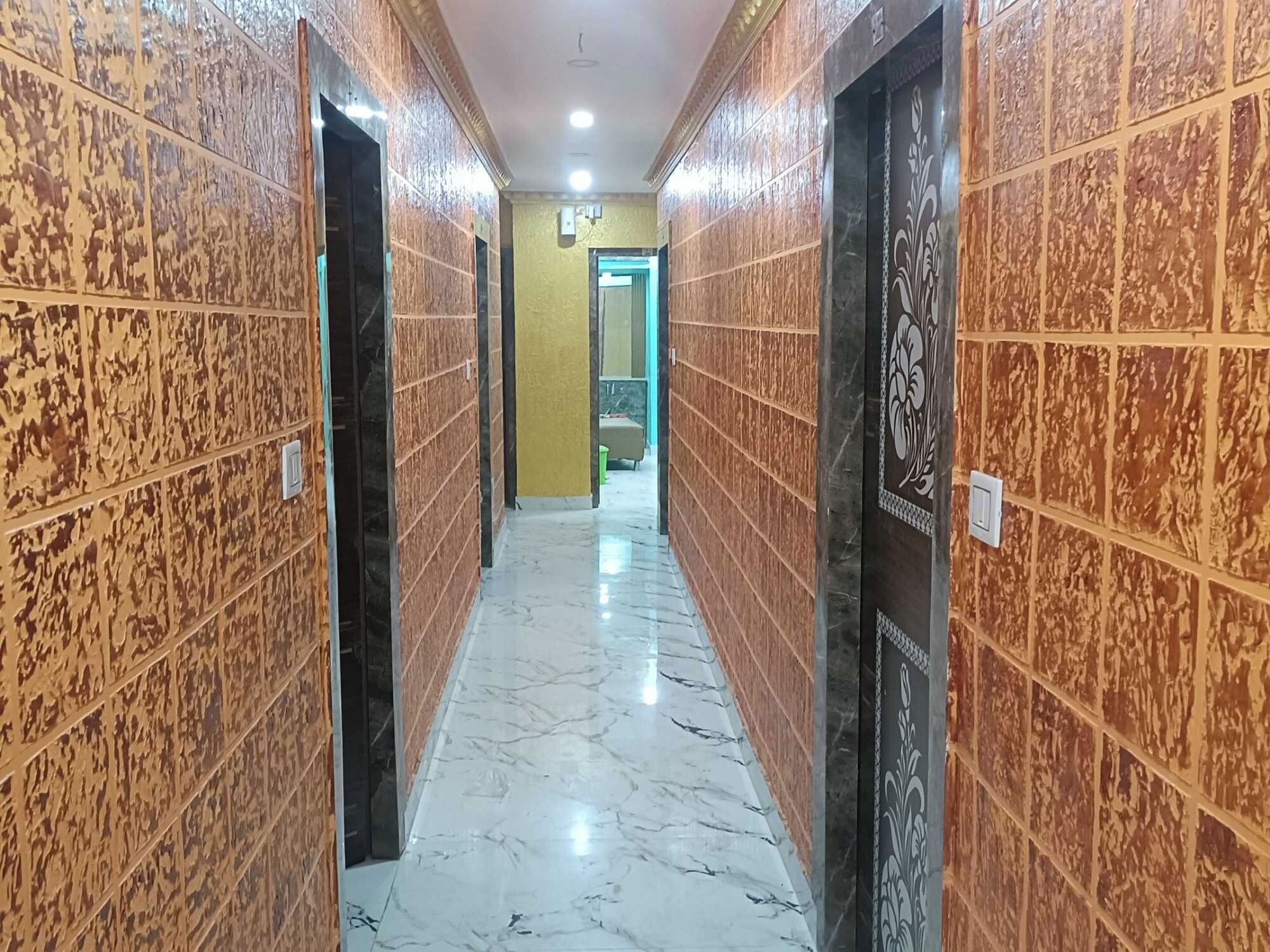 Un passadís amb terra de marbre i parets amb disseny, que condueix a una habitació amb una porta verda.