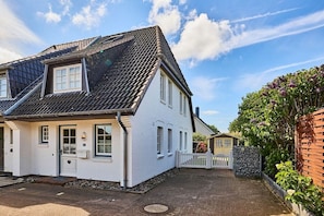 Ein zweistöckiges Haus mit Satteldach, einer Veranda und einem kleinen Garten.