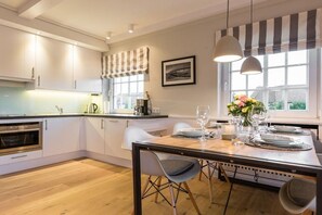A modern kitchen with white cabinets, a dining table set for four, and a large window with a view. - Luxury suite "Beach Style" under a thatched roof (Keitum)
