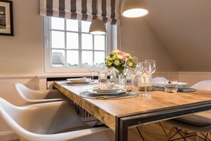 A dining area with a wooden table set for four, white chairs, and a window with a view. - Luxury suite "Beach Style" under a thatched roof (Keitum)