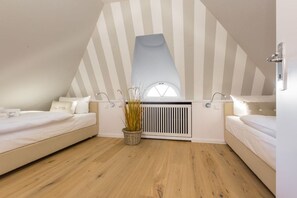A bedroom with two beds, a radiator, and a window. - Luxury suite "Beach Style" under a thatched roof (Keitum)