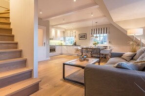 A modern kitchen with a dining area, a staircase, and a living room with a sofa and coffee table. - Luxury suite "Beach Style" under a thatched roof (Keitum)