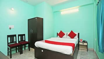A hotel room with a bed, a wardrobe, two chairs, a bedside table with a phone, and a blue curtain.