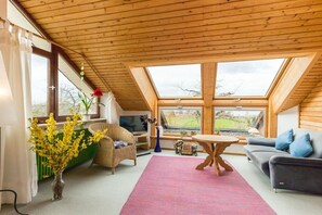 A cozy living room with a sloped ceiling, a sofa, a table, and a large window offering a view of the outdoors. - Holiday apartment with 1 bedroom (Meersburg)