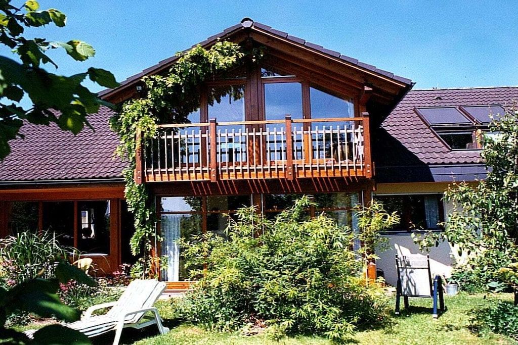 A two-story house with a balcony, surrounded by greenery and a garden.