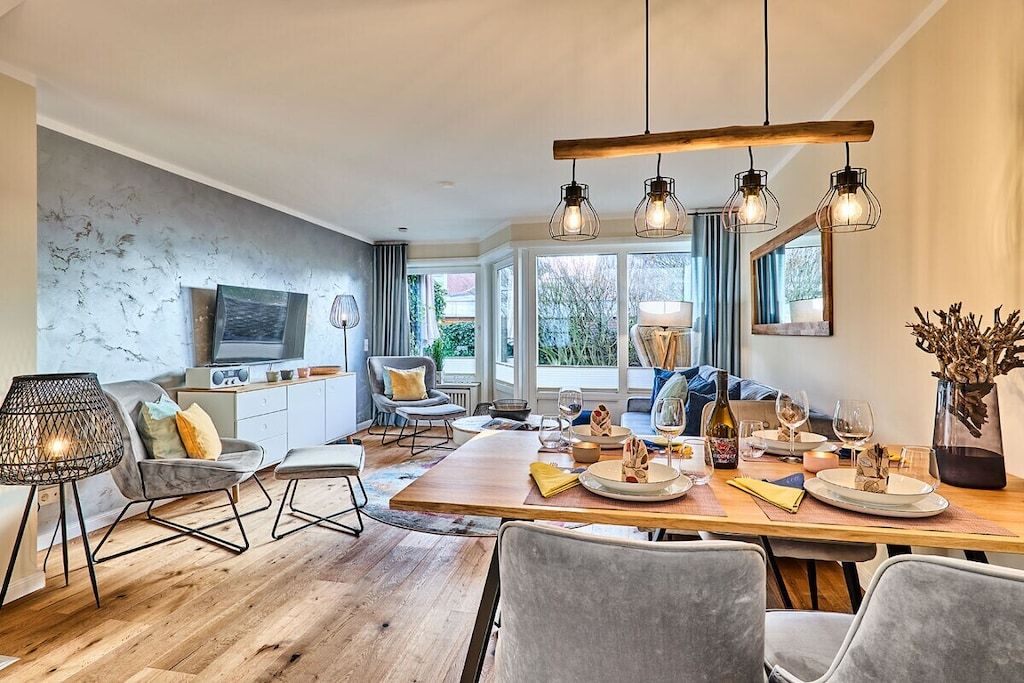 Un espace de repas moderne avec une table en bois dressée pour un repas, un canapé et un téléviseur en arrière-plan.