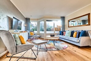 A modern living room with a sofa, armchair, and coffee table, large windows, and a view of the outdoors. - Holiday home with 3 bedrooms (Westerland)