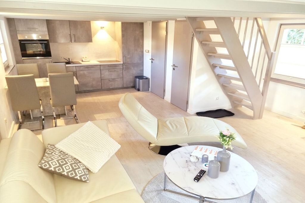 A compact living space with a sofa, a round coffee table, a kitchen area, and a staircase.