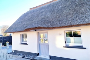 A single-story house with a thatched roof, a white exterior, and a small porch area. - Holiday home in Zingst with swimming pool (Zingst)