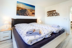 A bedroom with a bed, nightstands, a wall-mounted artwork, and a decorative wall piece. - Villa by the sea, Apt. 7 (St. Peter-Ording)