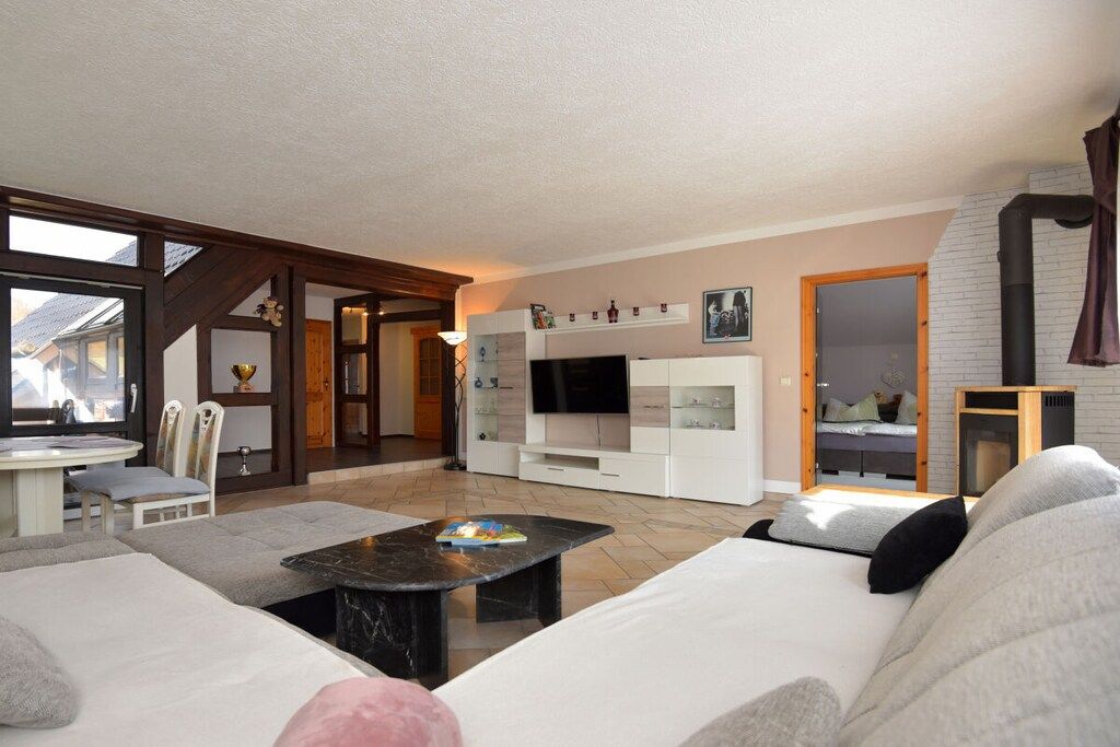 A modern living room with a sofa, a coffee table, and a TV. There is a fireplace and a window with a view.