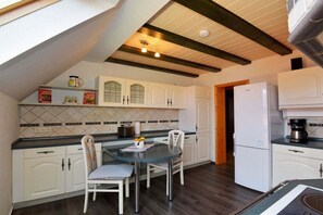 A kitchen with white cabinets, a dining table with chairs, a refrigerator, and a coffee maker. - Holiday apartment in Waltershausen with Wi-Fi (Waltershausen)
