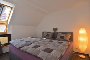 A bedroom with a bed, a nightstand, a lamp, a window, and a wall decoration. - Holiday apartment in Waltershausen with Wi-Fi (Waltershausen)