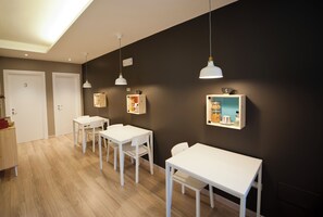 Ein Zimmer mit zwei weißen Tischen und Stühlen, einer dunklen Wand und einem Holzboden.