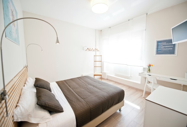 Ein Schlafzimmer mit Bett, Nachttischlampe und Schreibtisch mit Stuhl.