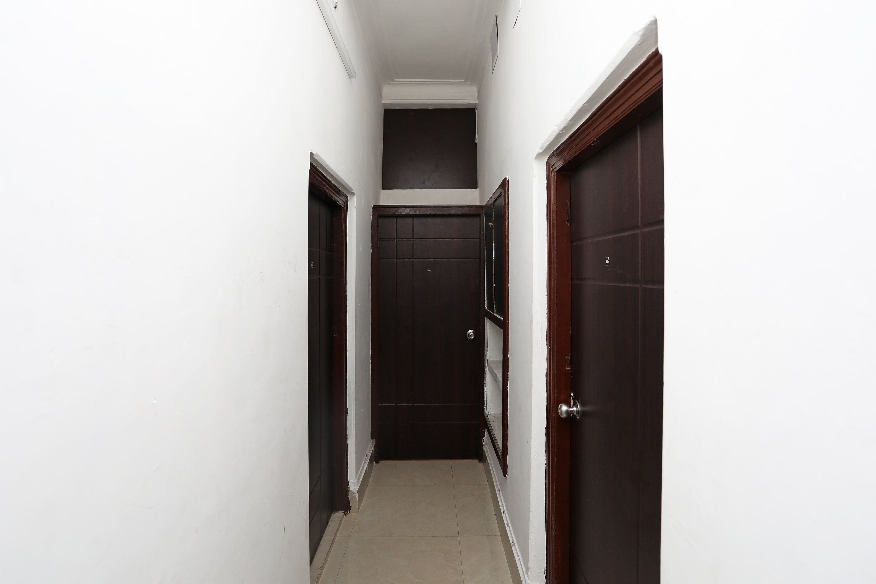 Un couloir étroit aux murs blancs et aux portes en bois foncé.