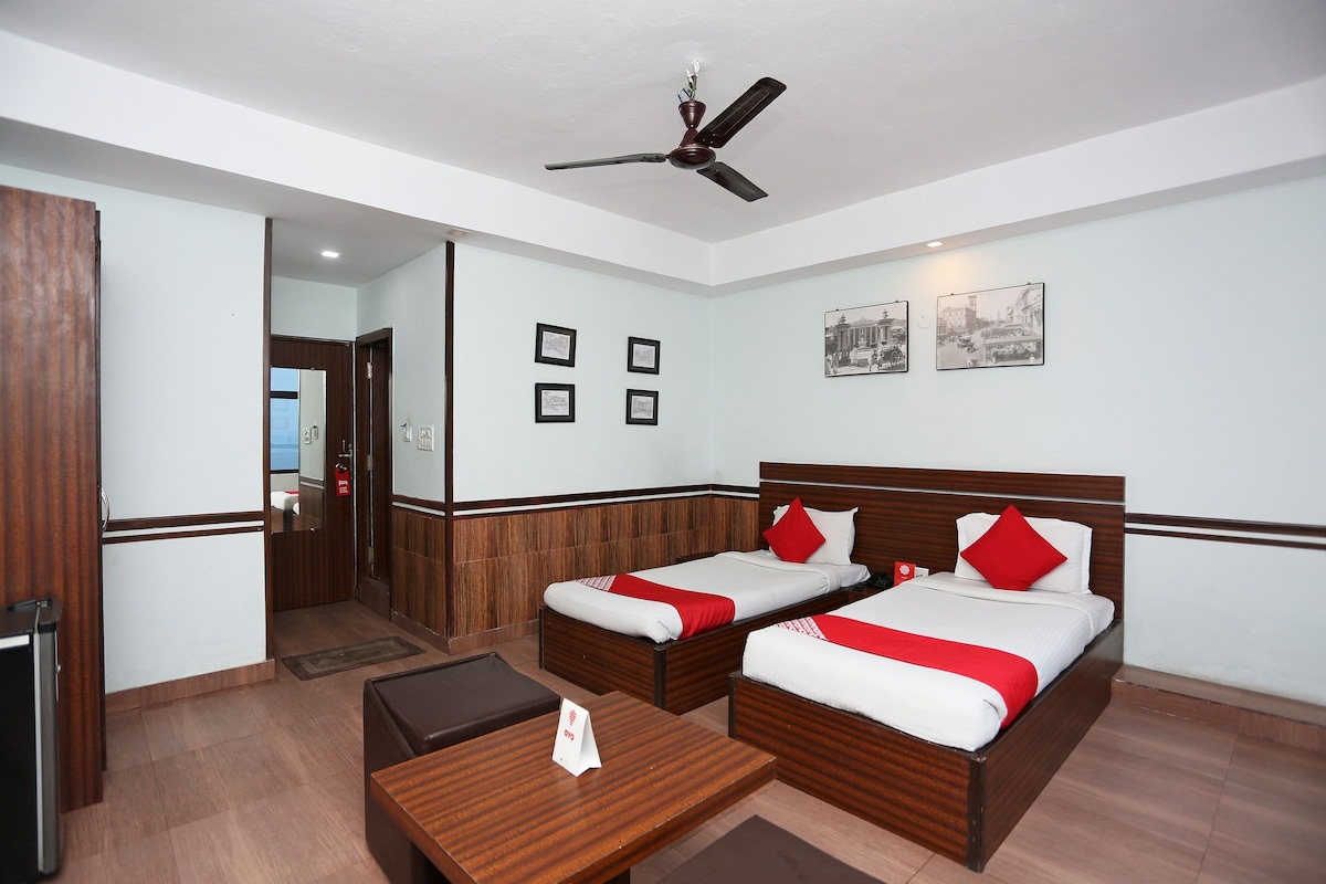 A hotel room with two beds, a desk, a ceiling fan, and framed pictures on the wall.