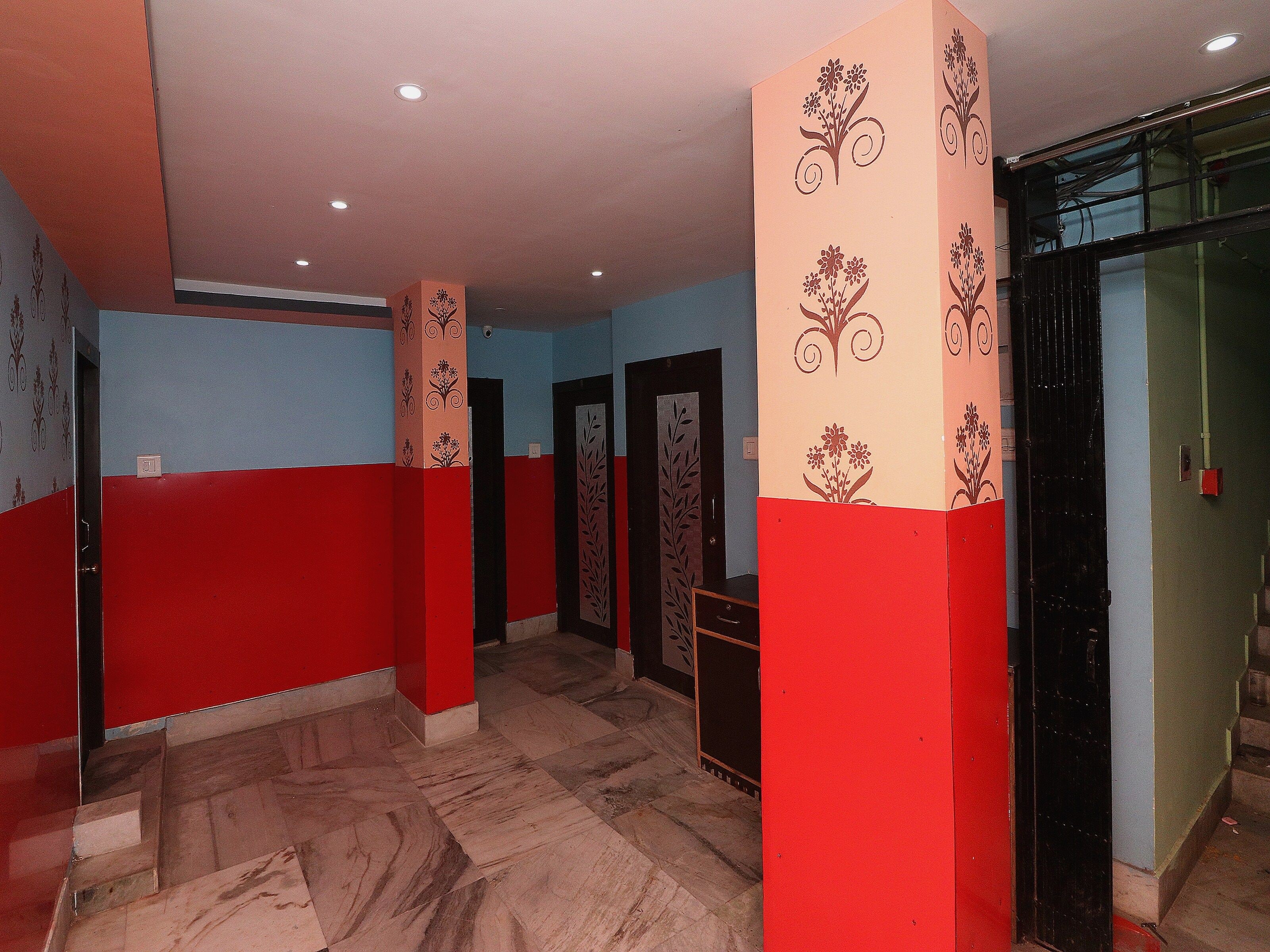 Un pasillo con paredes rojas y azules, suelo de mármol y columnas decorativas.