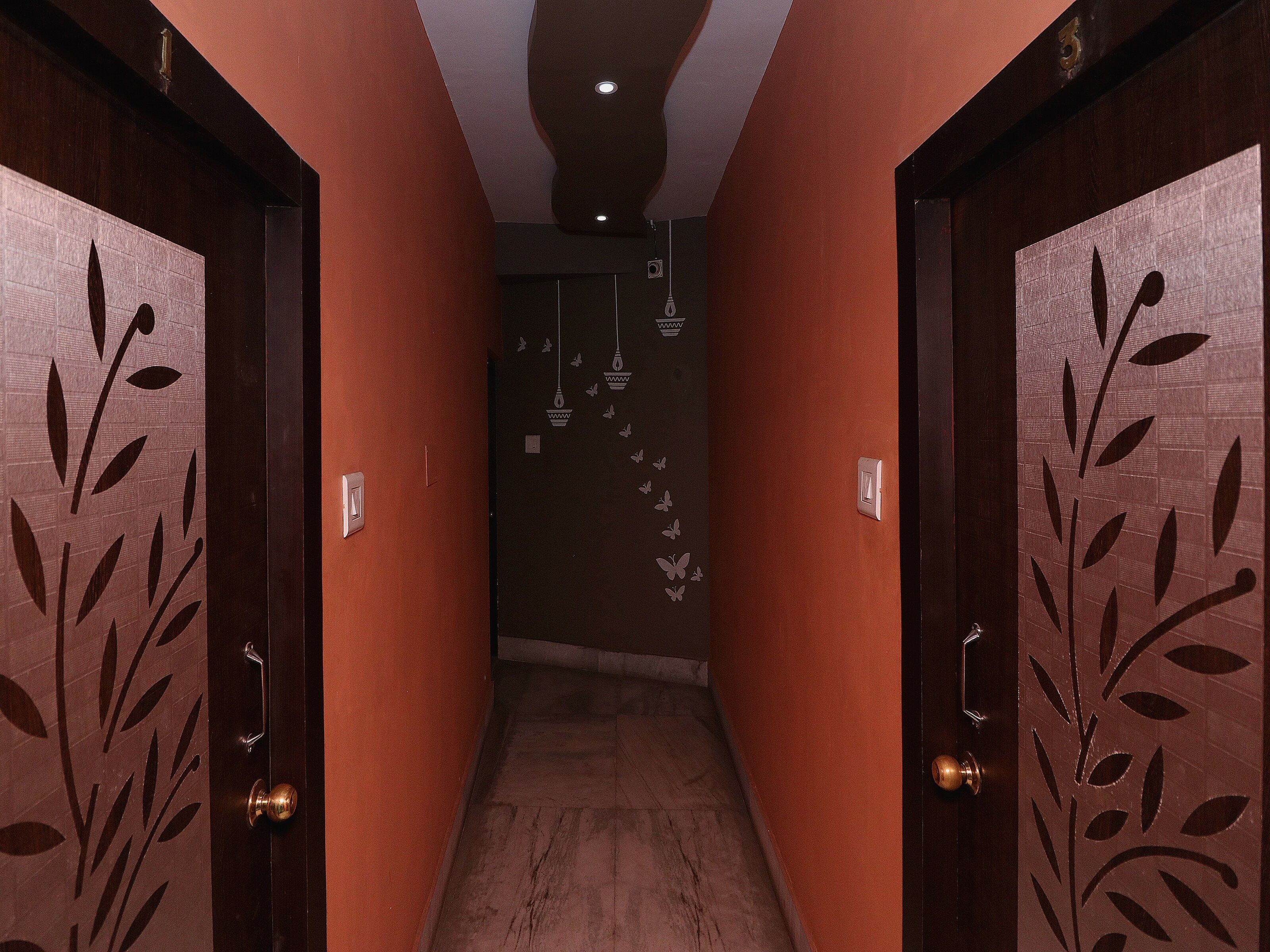 Un pasillo con puertas de madera decoradas con motivos de hojas, una lámpara y una pared con un adhesivo de mariposa.