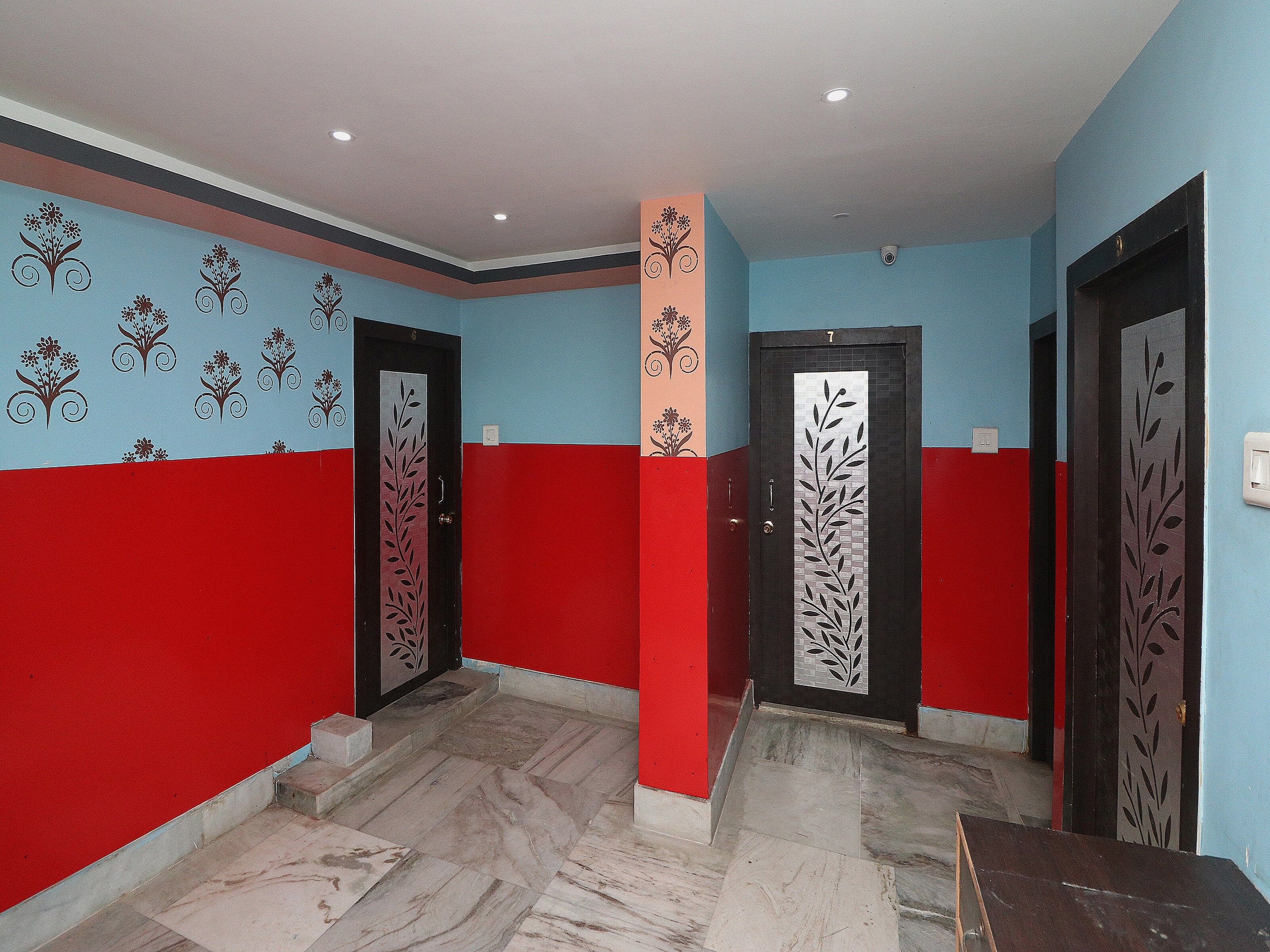 Un pasillo con paredes rojas y azules, dos puertas con diseños decorativos y un suelo de baldosas.