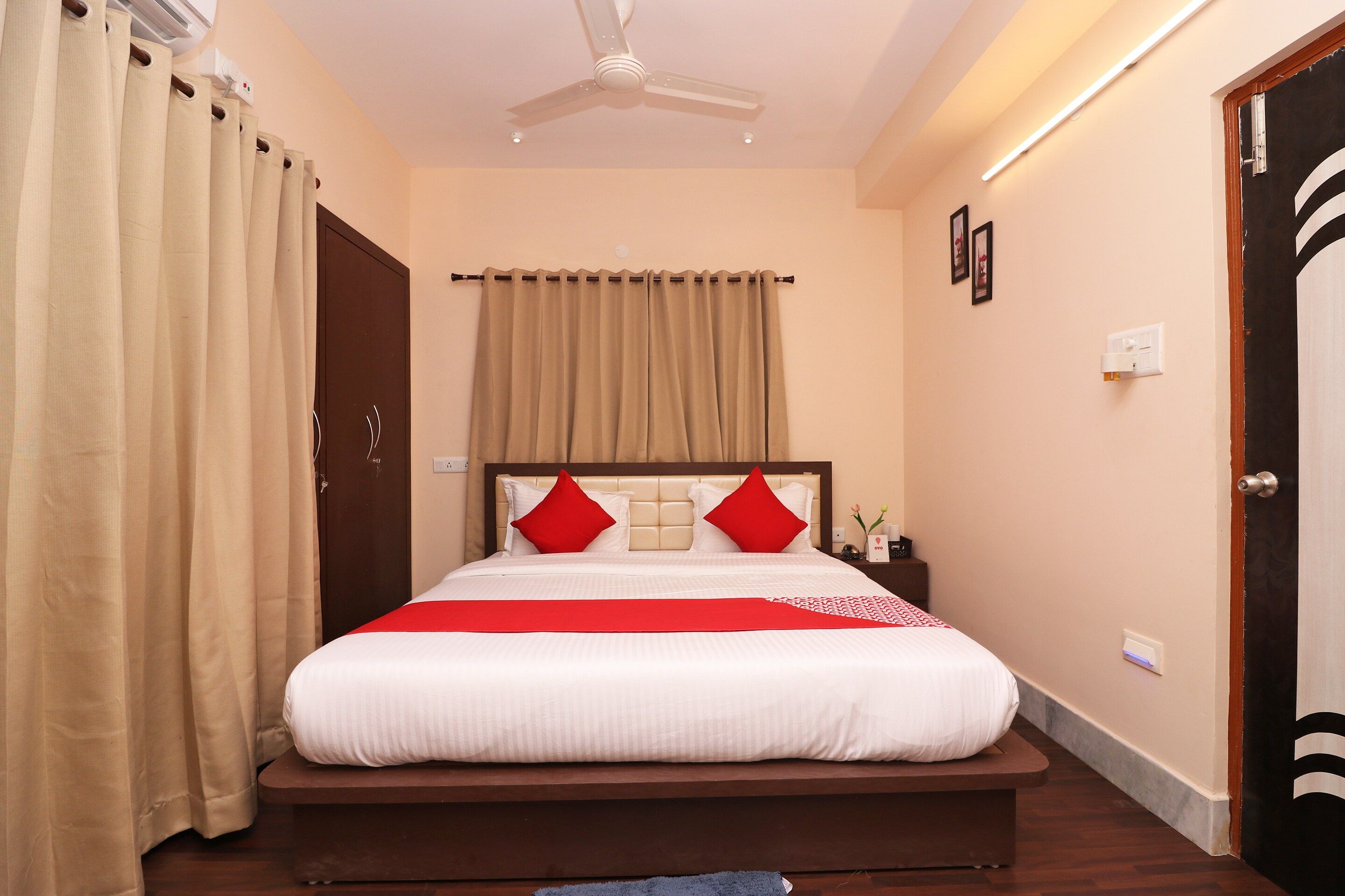 A hotel room with a bed, curtains, a ceiling fan, and a nightstand with a vase.