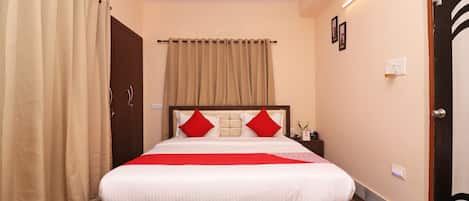 A hotel room with a bed, curtains, a ceiling fan, and a nightstand with a vase.
