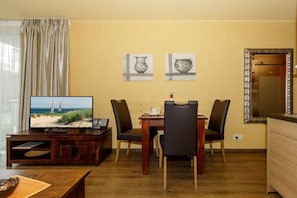 A dining area with a wooden table and four chairs, a television on a wooden stand, and two framed artworks on the wall. - Holiday apartment Villa Patricia 319561 (Kühlungsborn-Ost)