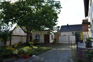 A courtyard with a cobblestone path, a tree, and a building with a door and window. - Holiday apartment with 3 bedrooms (Strullendorf, Germany)