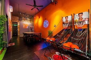 A basketball arcade with a neon sign, a basketball hoop, and a seating area with tables and chairs.