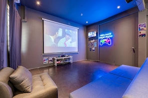 A home theater room with a large screen, comfortable seating, and a neon sign indicating a game room.