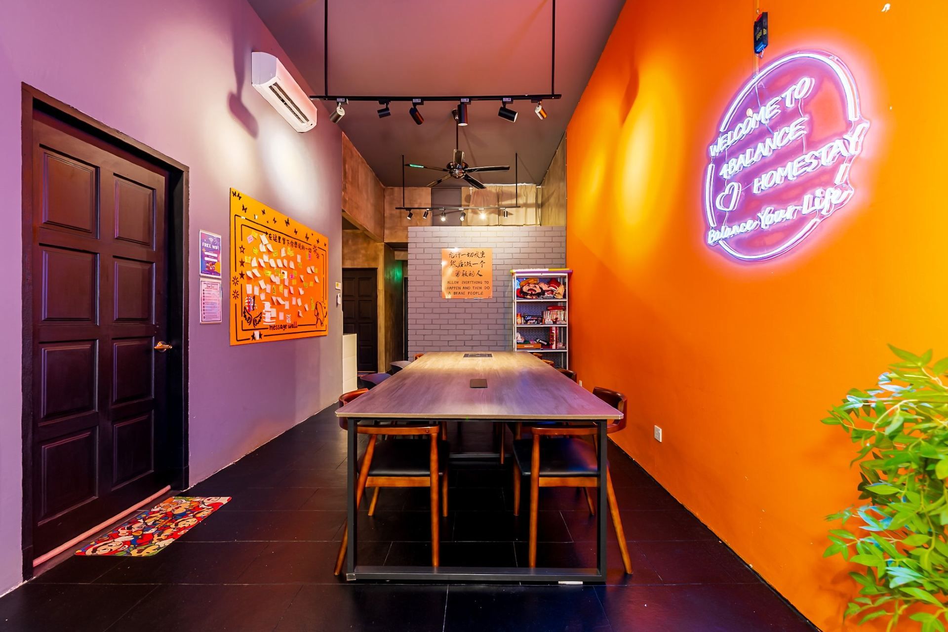 A conference room with a long table and chairs, a neon sign on the wall, and a message wall with sticky notes.