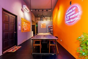 A conference room with a long table and chairs, a neon sign on the wall, and a message wall with sticky notes.