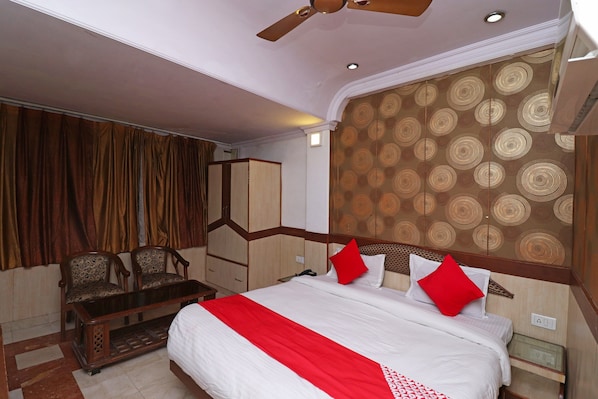 A hotel room with a bed, a desk, two chairs, a wardrobe, and a patterned wall.