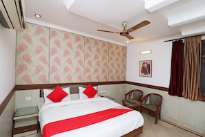A hotel room with a bed, two chairs, a ceiling fan, and a window with curtains. - Hotel O by OYO Highway Inn International (Kolkata)