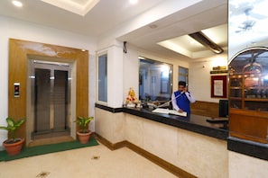 A hotel reception area with a receptionist, an elevator, and a reception desk.
