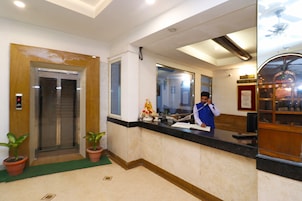 Zona de recepción de un hotel con recepcionista, un ascensor y mostrador de recepción.