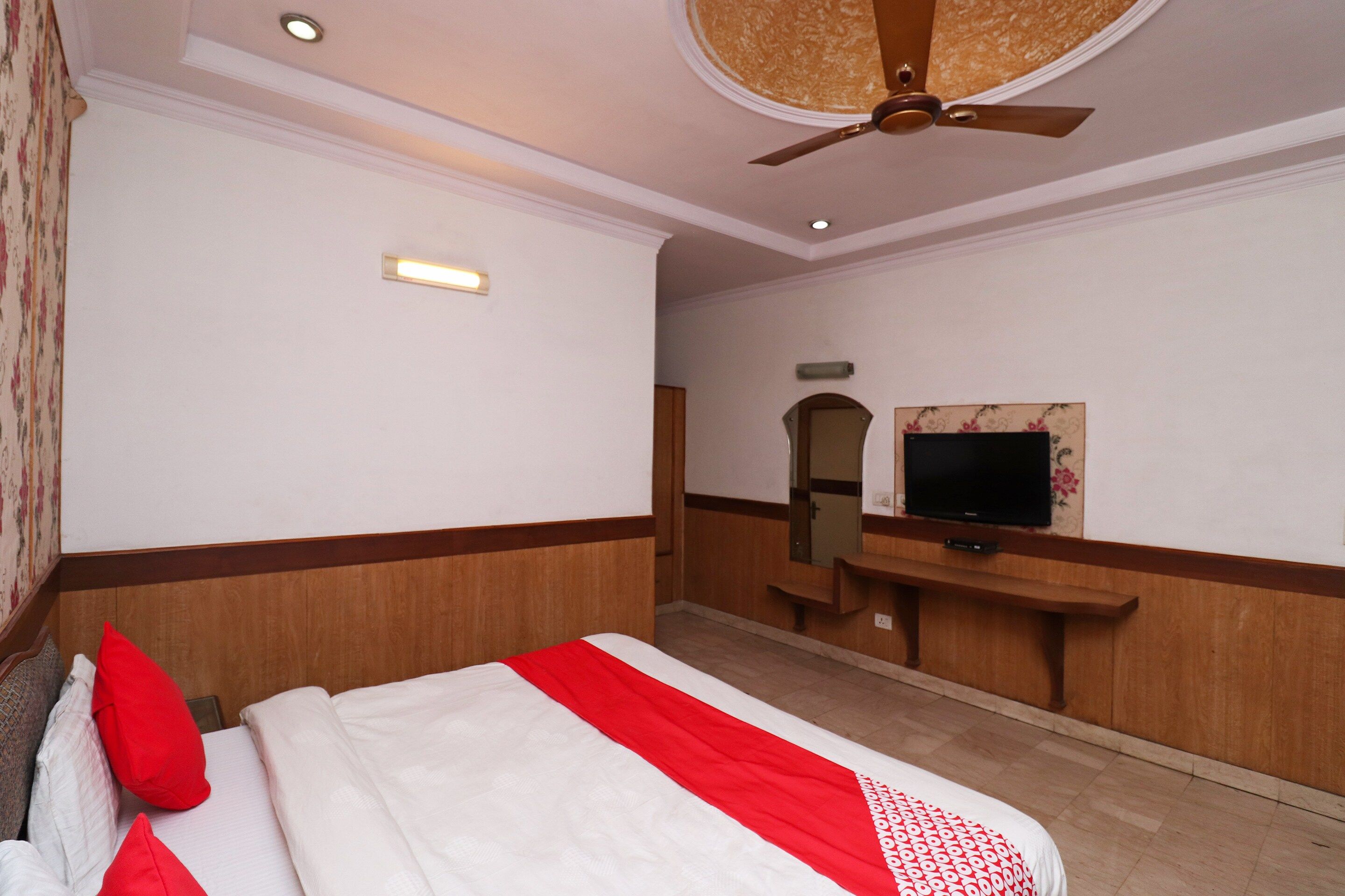 Una camera d'albergo con un letto, una televisione, uno specchio e una ventola a soffitto.