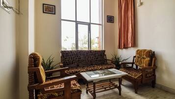 Una sala de estar con un sofá, dos sillones, una mesa de centro y un ventanal con cortinas.