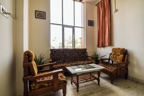Een woonkamer met een bank met stenen motief, twee houten fauteuils, een glazen salontafel en uitzicht op de natuur door grote ramen.