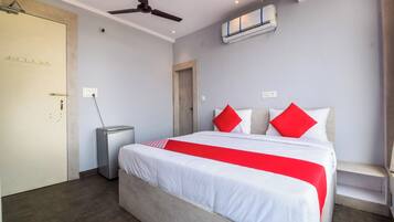 Una habitación de hotel con una cama, un ventilador de techo, un equipo de aire acondicionado, una mesita de noche y una puerta.