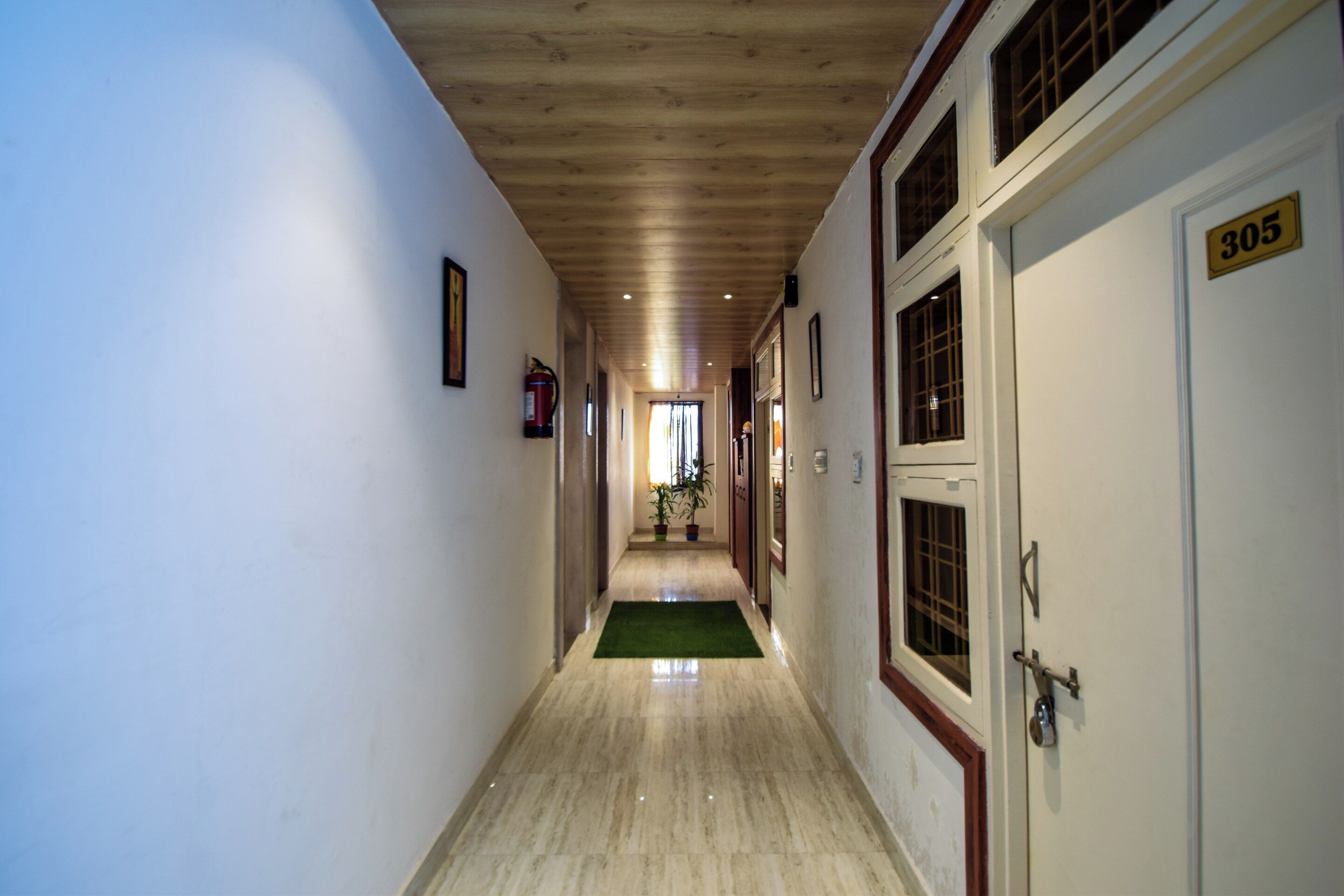 Un pasillo con techo de madera, un felpudo verde al final y una puerta con la etiqueta '305'.