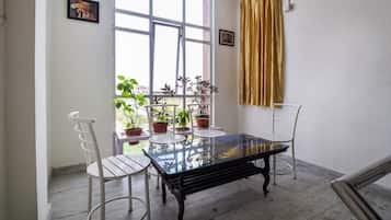 A room with a glass-top table, two white chairs, a window with curtains, and potted plants.