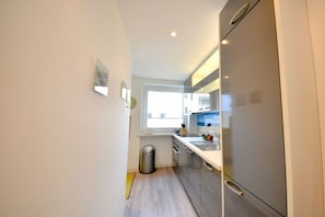 A compact kitchen with a stainless steel refrigerator, a window, and a trash bin. - House Poseidon - Apartment 2.1 (Wangerooge)