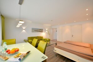 A modern hotel room with a glass dining table, a sofa, a bed, and a wall-mounted light fixture. - House Poseidon - Apartment 2.1 (Wangerooge)