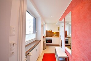 A compact kitchen with white cabinets, a red rug, and a window providing natural light. - House Poseidon - Apartment 1.1 (Wangerooge)